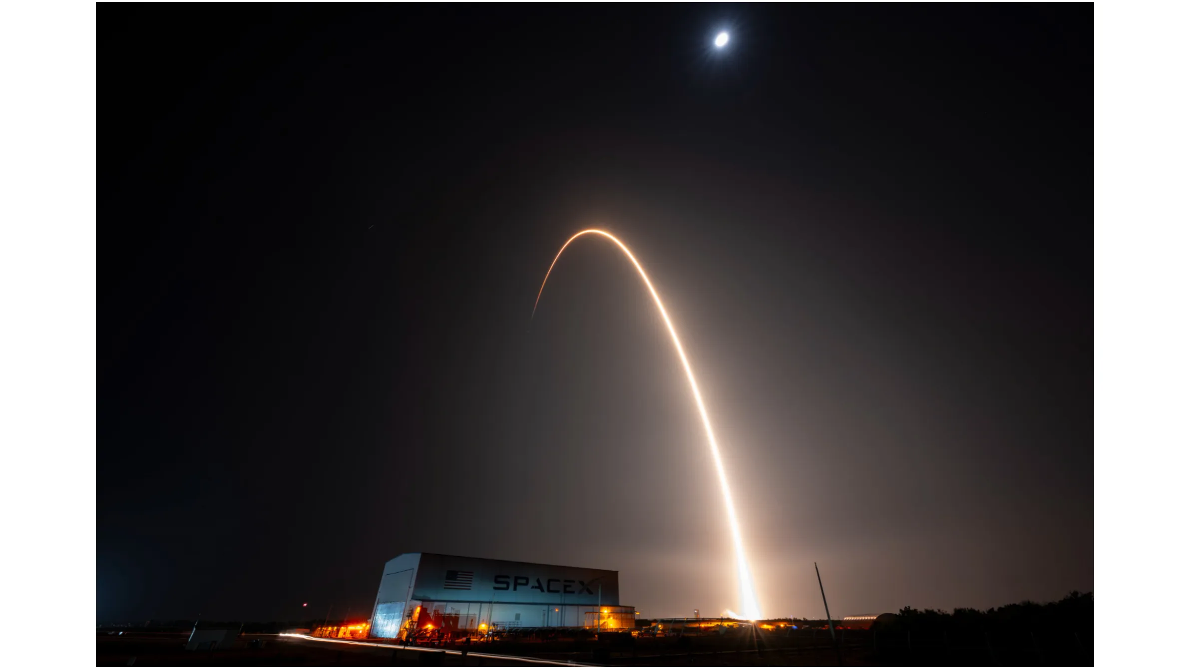 Ein Raketenstart zeichnet einen orangefarbenen Bogen in den dunklen Nachthimmel auf diesem Langzeitbelichtungsfoto.